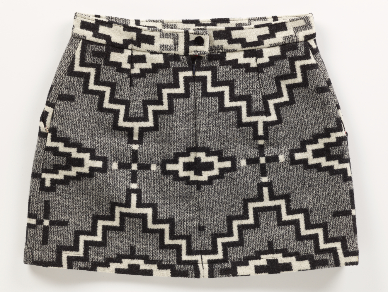 Gray tweed skirt with black and white geometric pattern throughout. The top of the skirt is a lighter gray with a singular black button in the center. 