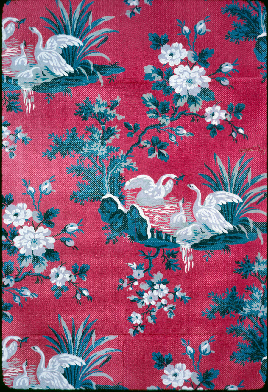 Segment of vintage wallpaper featuring a pattern of bright white cranes within idyllic pond scenes. The vignettes are decorated with blue floral motifs on a deep red background.