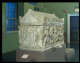 View of the whole sarcophagus in a gallery. The rectangular sides feature carvings of the Trojan war. The triangular lid is adorned with carved lion heads and floral details.