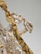 Close-up of a silver figure in robes with a thin gold sash and flowing, wavy hair entangled in her fingers and an arcing gold, rosy, leafy garland crossing her face. 