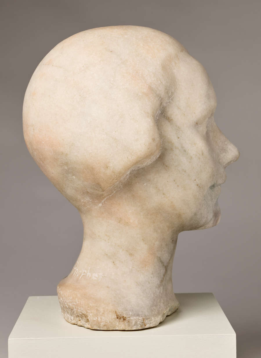 Three quarter back view of marble sculpture depicting the head of a female figure. The head features a short hairstyle, close to the scalp, while the face holds a subtle expression.