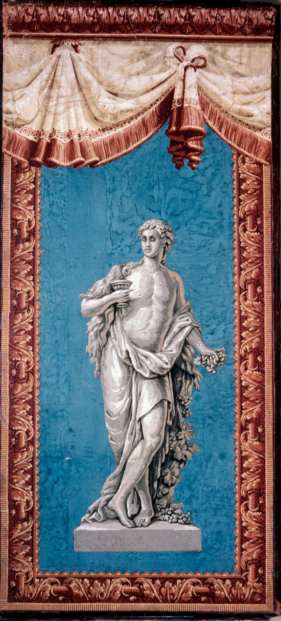 Sculptural figure draped in flowing robes holding a cup in one hand and a wheat bundle in the other. An elaborate terracotta border frames the figure and the blue background.