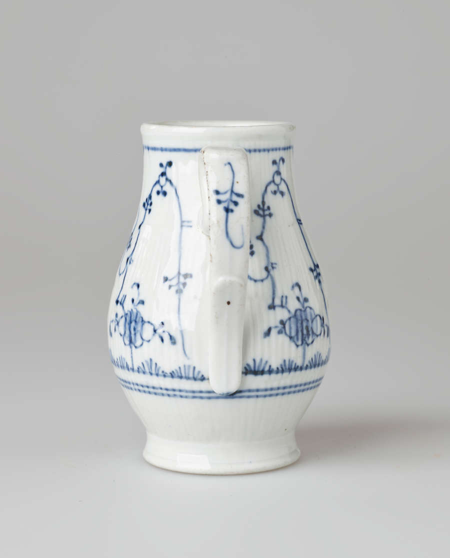 A white chocolate pot with delicate blue decorations with ribbed body, spout, handle, and foot.