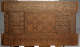 A close up of a rectangular wooden chest panel featuring intricate geometric carvings bordered by calligraphy and smaller intricate patterns. 
