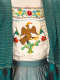 Blue fabric layers framing a white blouse with a central embroidered eagle atop a cactus framed by Mexican flags and colorful floral patterns tucked into a blue cinched waist band. 