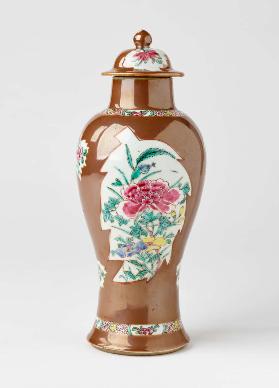 A brown and white covered vase with pink, green, blue, and yellow floral decorations.