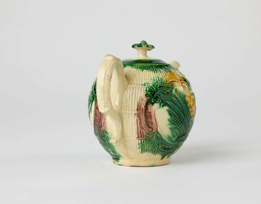 A bulbous teapot with white, green, and yellow floral decorations in the form of a leafy pineapple.