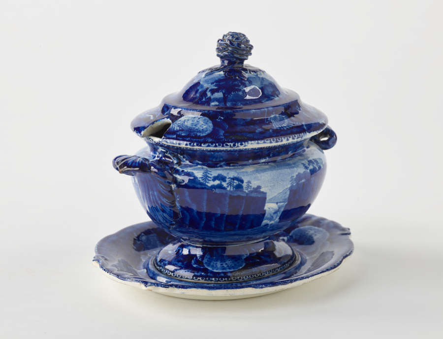  A dark blue decorative sauce boat. Two symmetrical sculptural handles that depict a bird’s head, foot, and lid with rounded finial