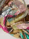 Close-up of densely knotted woven textiles coated in glittering pink, teal, gold, and silver. 
