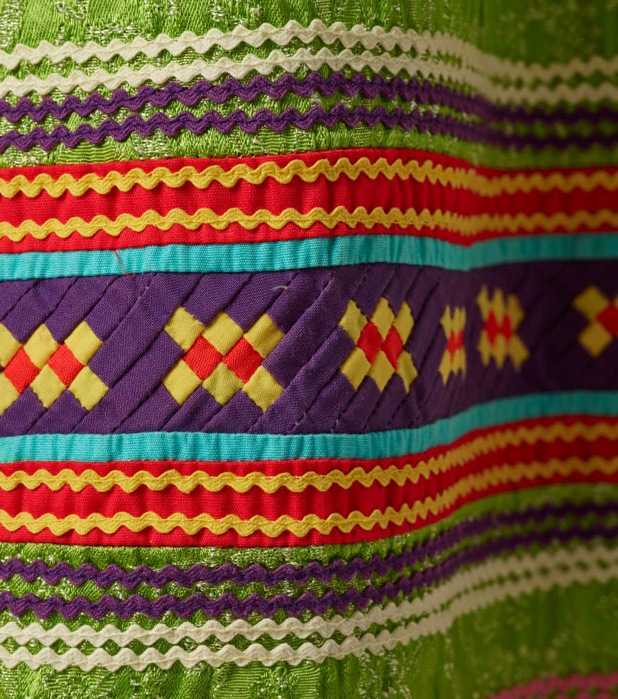 Another detail of the pattern. A thick strip of purple with yellow and red squares woven through it is surrounded by wavy horizontal red, yellow, green, white, and purple stripes. 

