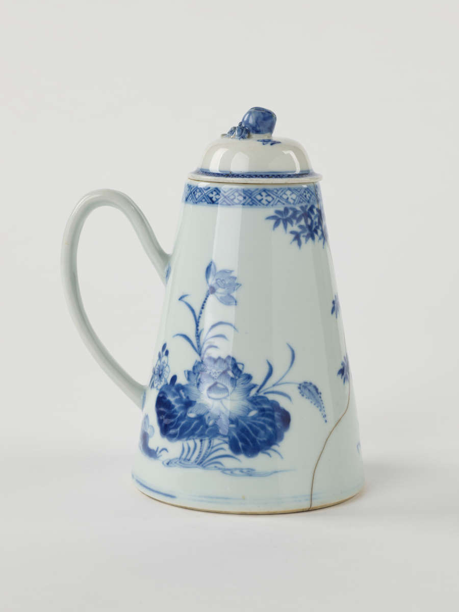 A white and blue teapot with floral decorations, a lid with a small semi spherical finial, spout, and a handle which is located approximately 90 degrees from the spout.