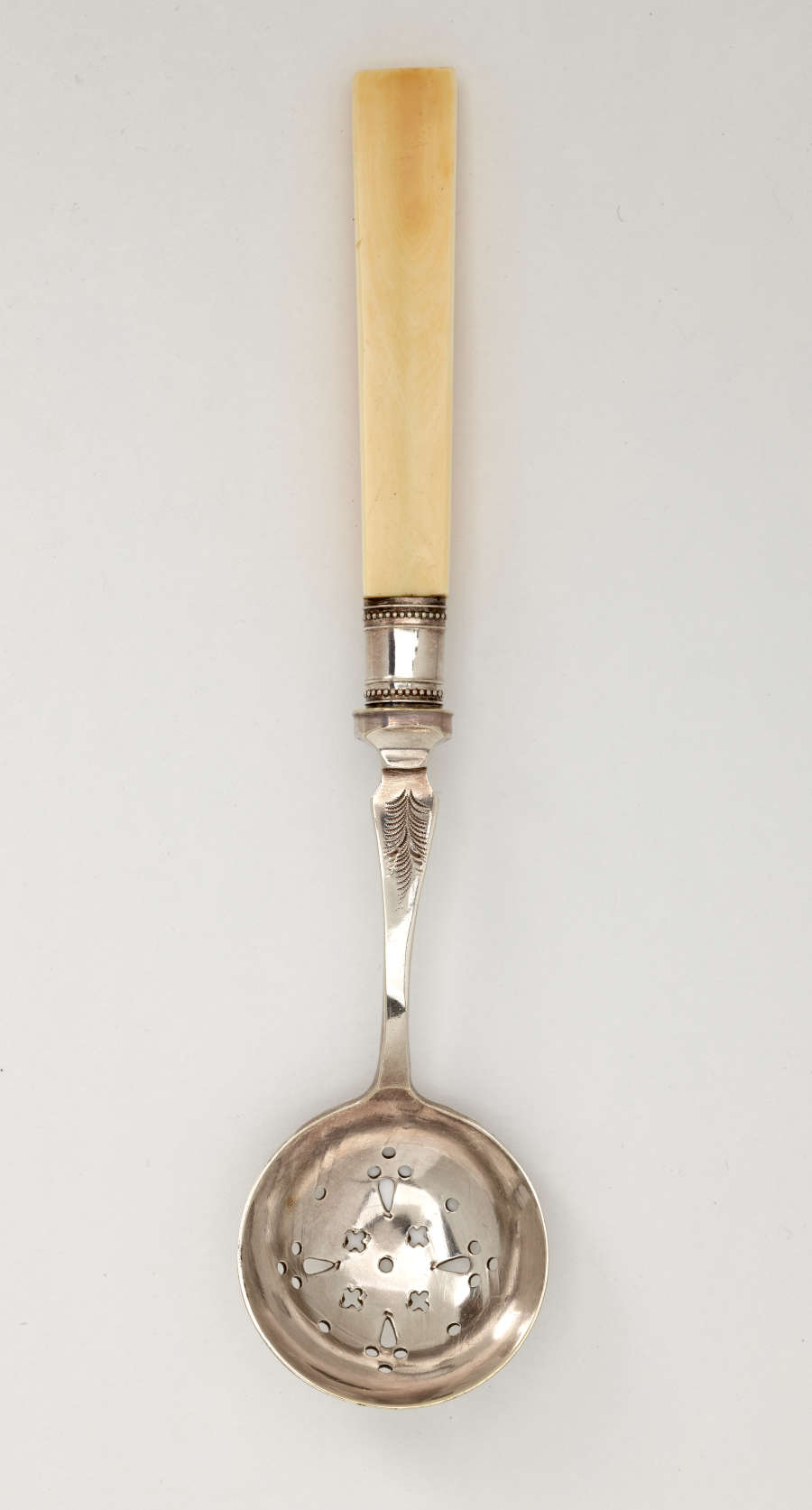 A metal tool with small cutouts in the bowl and an ivory handle.