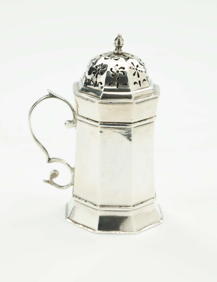  A silver vessel that has an octagonal body, handle, and lid that has floral perforations.
