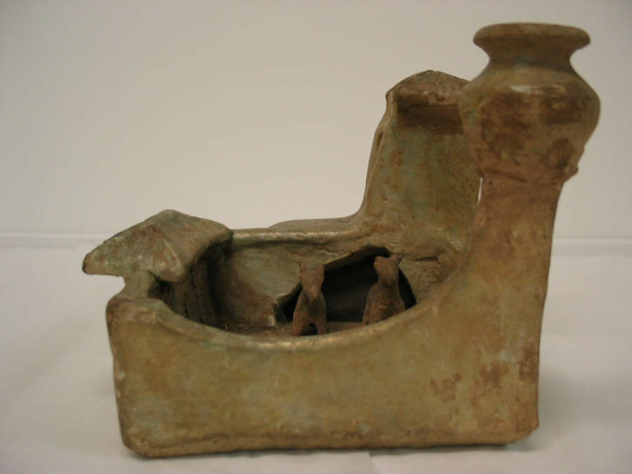 Side-view of a green-brown ceramic sculpture of a walled farmyard with a courtyard with two animals, a roofed entrance and two towers, one with an onion-shaped pot upon it.