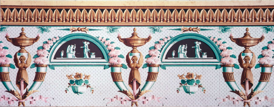 Decorative frieze featuring scenes within semi-circles surrounded by flowers alternating with bronze winged figures holding up urns. The color palette is a subdued mint, pink, bronze, and cream.