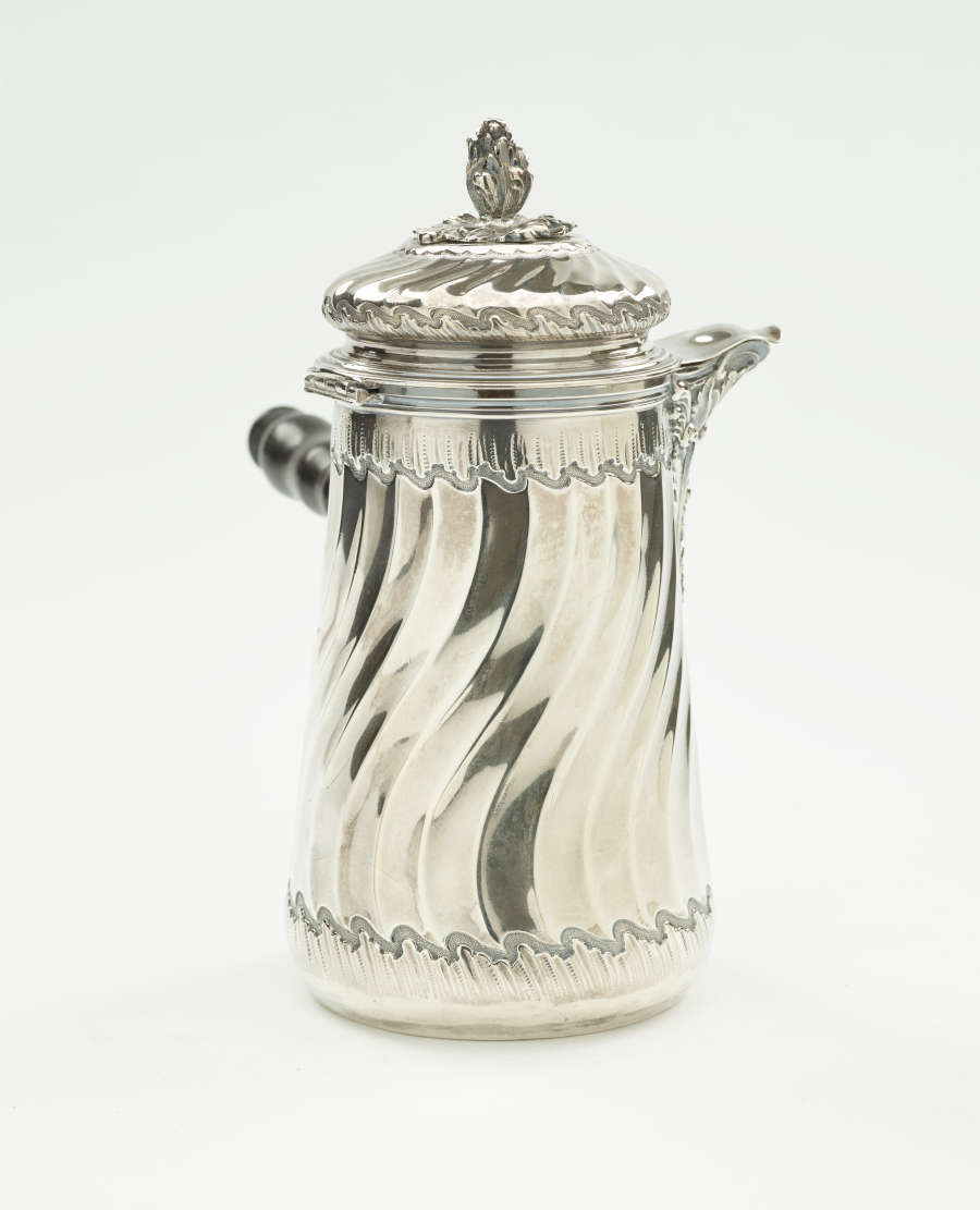 A silver chocolate pot with a decorative swirled body, lid, and fruit wood handle.