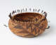 Woven tan and brown onion shaped bowl with geometric dark brown patterning and feather-like tassels emerging from the top edge of the bowl.