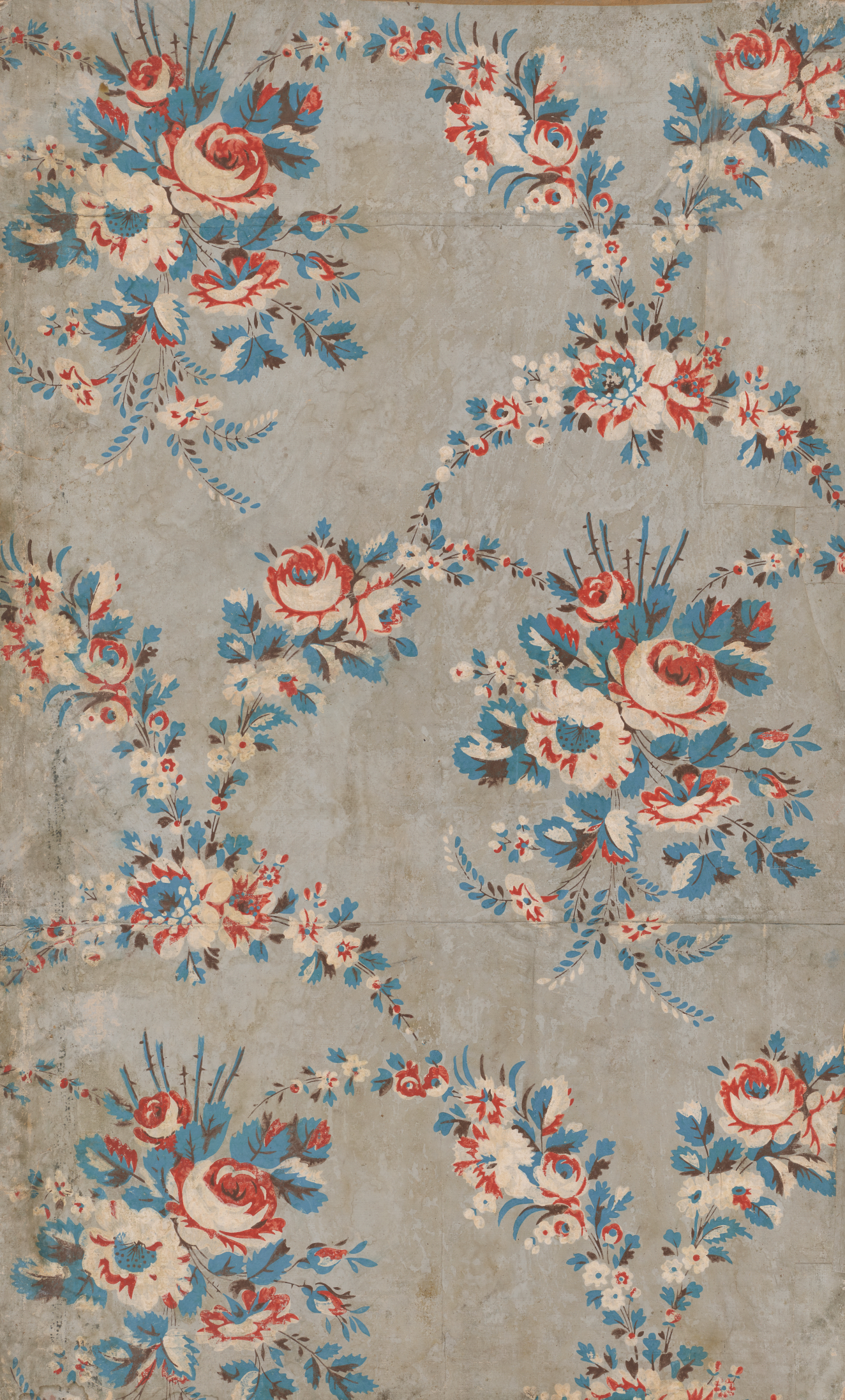 Panel of vintage wallpaper featuring a classic linking floral pattern with vibrant red roses and blue accents on a gray distressed background.