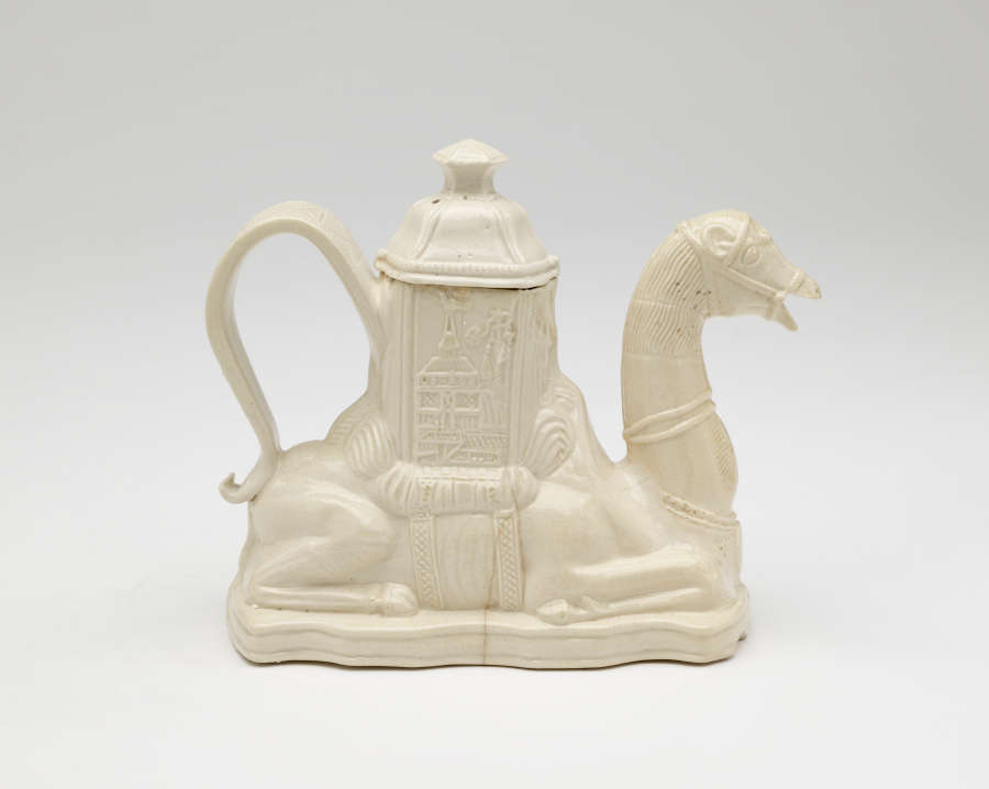 A cream colored teapot in the shape of a camel with a hexagonal lid.