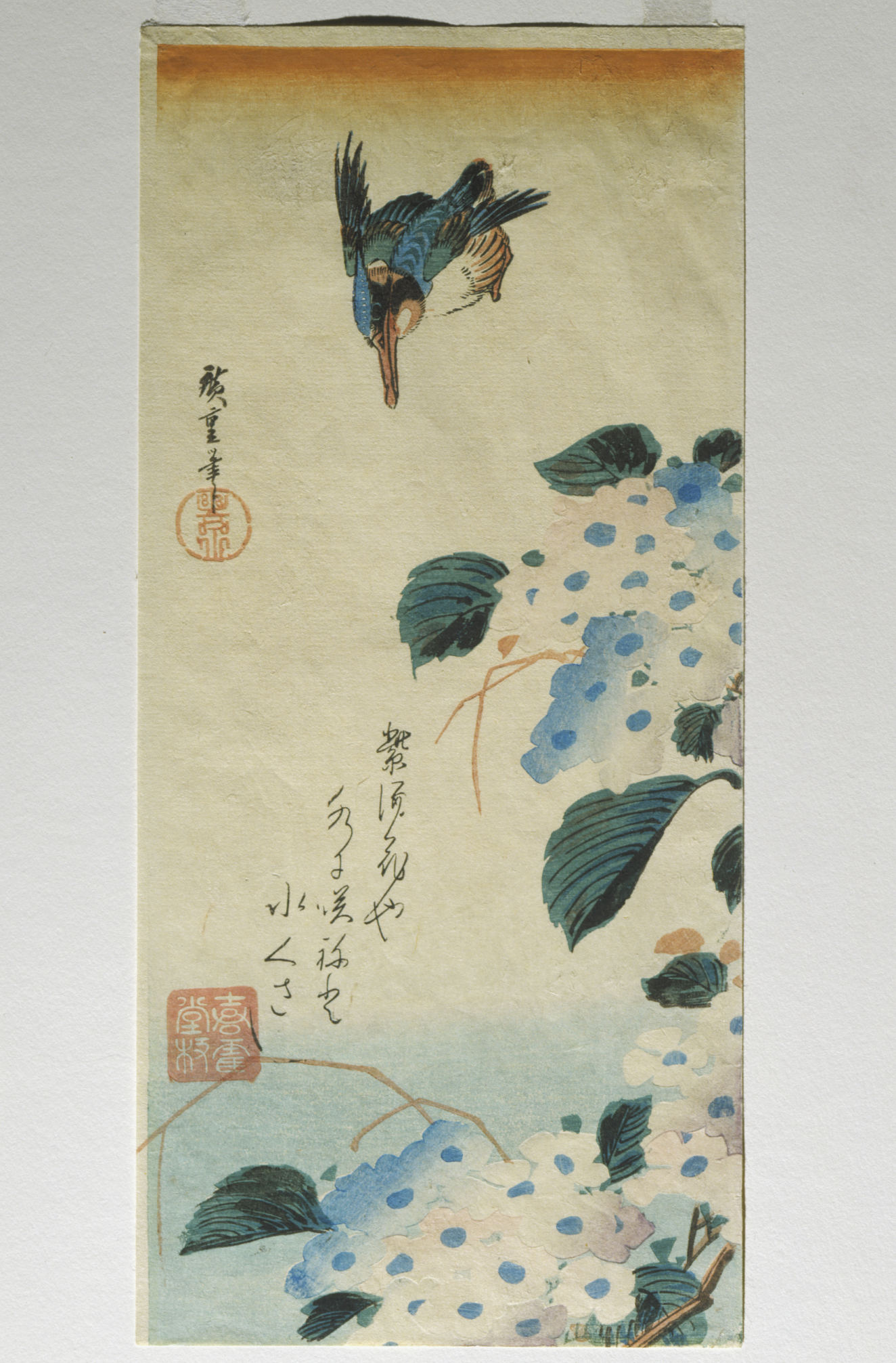A diving bird headed towards clusters of blooming blue hydrangeas with broad green leaves, and vertical calligraphy against a faded orange-to-blue sky.
