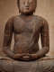 A close up of a seated wooden Buddha statue with its hands resting in its lap and visible signs of age and repair.