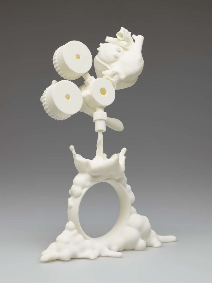 White plastic sculpture. At the top are suspended mechanical objects and an anatomical heart attached above right. A liquid-like form pours out from the machinery and over a standing bracelet.