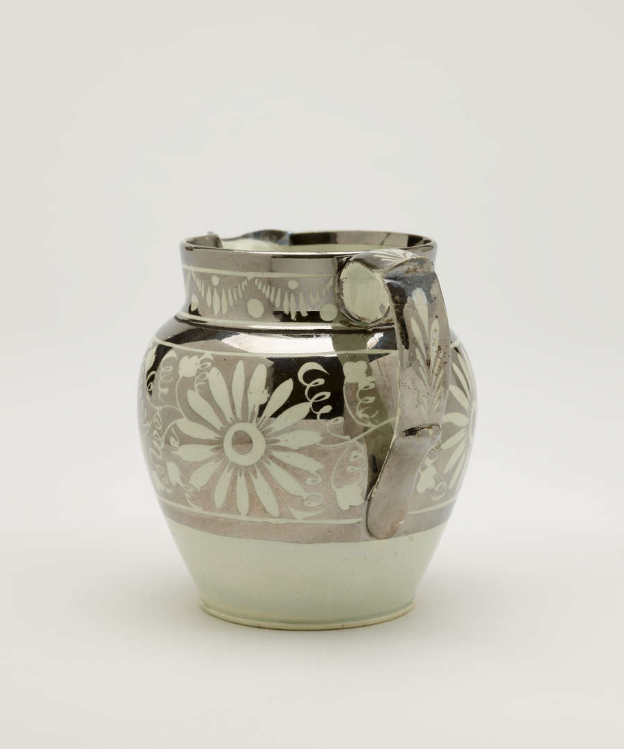 A silver-colored jug with floral motifs on the body of the vessel.