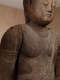 Close up of a weathered wooden Buddha statue, showing its serene expression and torso. 