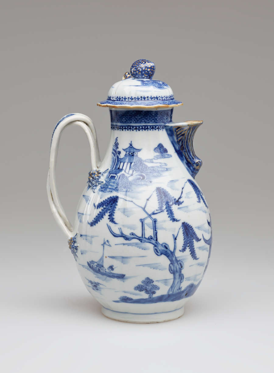A white and blue chocolate pot with a spout, handle, and lid, the edges of the lid and spout are gilded. The decorations mainly depict floral, architectural, and landscape elements.