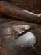 Close-up of a weathered wooden Buddha statue’s lap, highlighting a carved foot with exposed wood, resting on the carved folds of drapery.