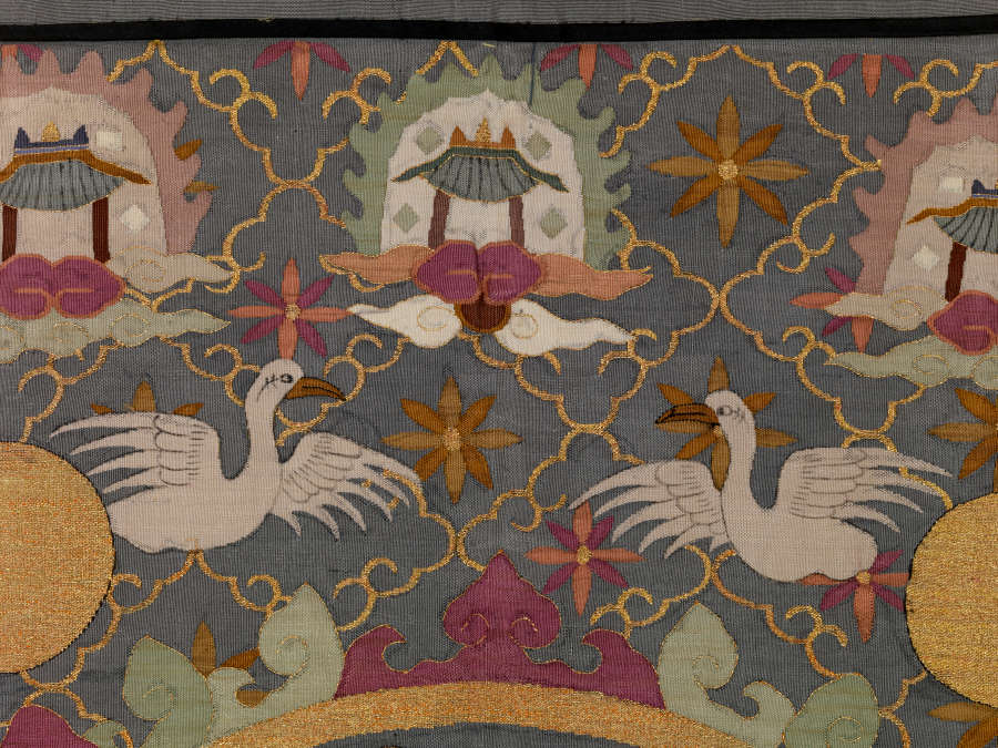Robe’s back detail, showing a symmetrical arrangement of two flaming and haloed pagodas above two white flying birds and golden circles, against a dark background with a thin diagonal grid.