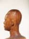 Close-up, three quarter back view of a textured, but glossy, wooden-carved bust depicting a male figure. The base and neck is blurred, highlighting the details in the head.