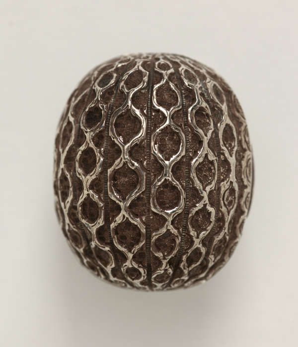 A silver nutmeg grater that is abstractly shaped like a nutmeg.