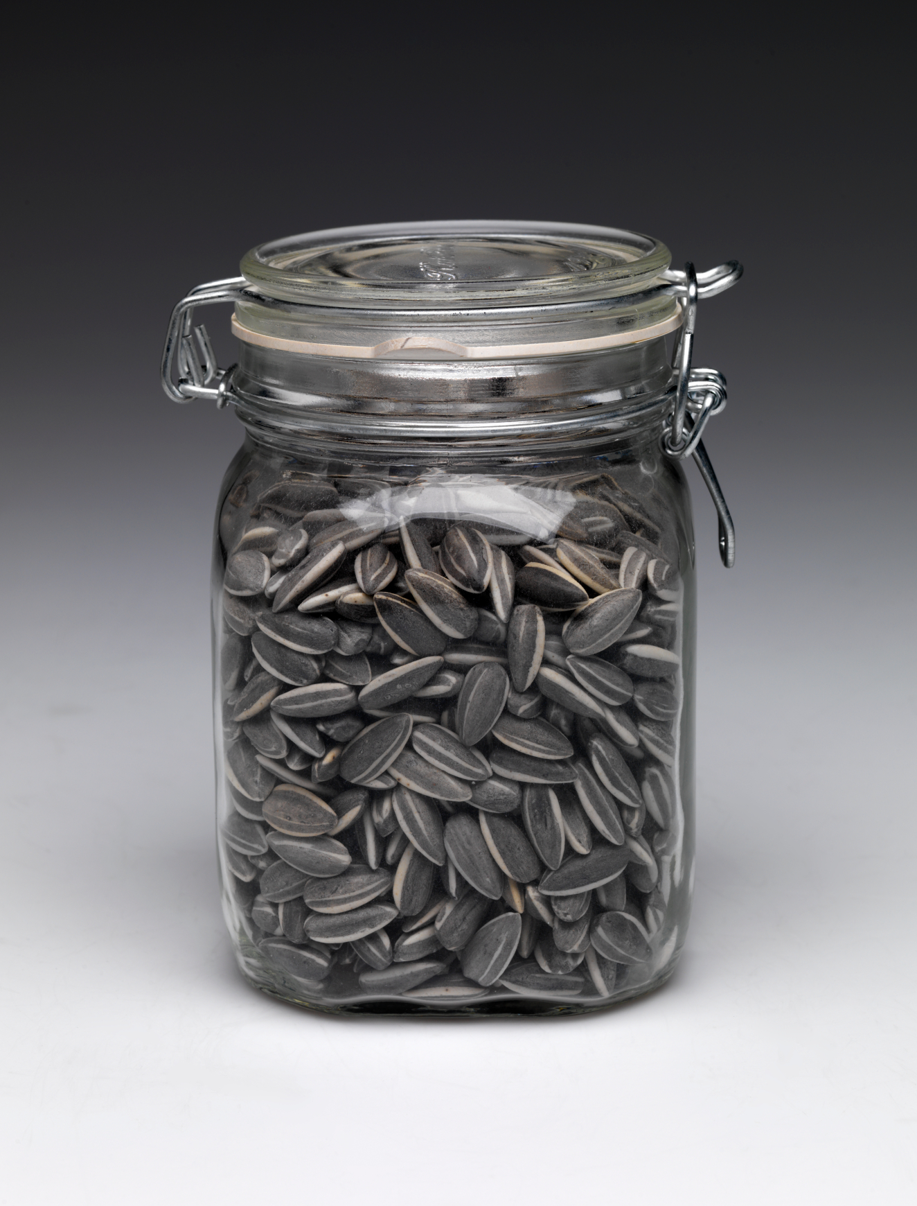 A glass jar tightly packed with gray and white striped sunflower seeds, sealed with a hinged metal clasp and a glass lid.