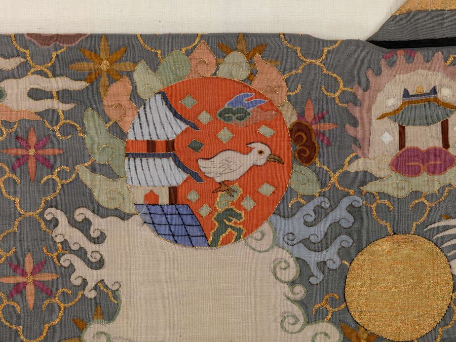Robe’s back detail, featuring a pagoda beside a white bird contained within a red circle, surrounded by earthy pastel clouds, against a dark background with a thin diagonal grid.