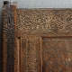 A close-up of an intricately carved wooden panel with calligraphic script along the top edge, with interwoven floral motifs and geometric star formations below. 