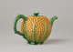 A teapot in the shape of a pineapple. Handle, foot, lid, and spout are green.