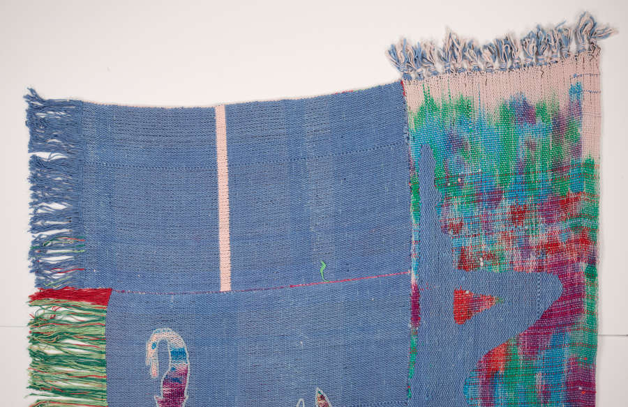View of another half of the tapestry. This one is mostly blue leaving one patterned edge with a blue silhouette of a recumbent man’s legs.