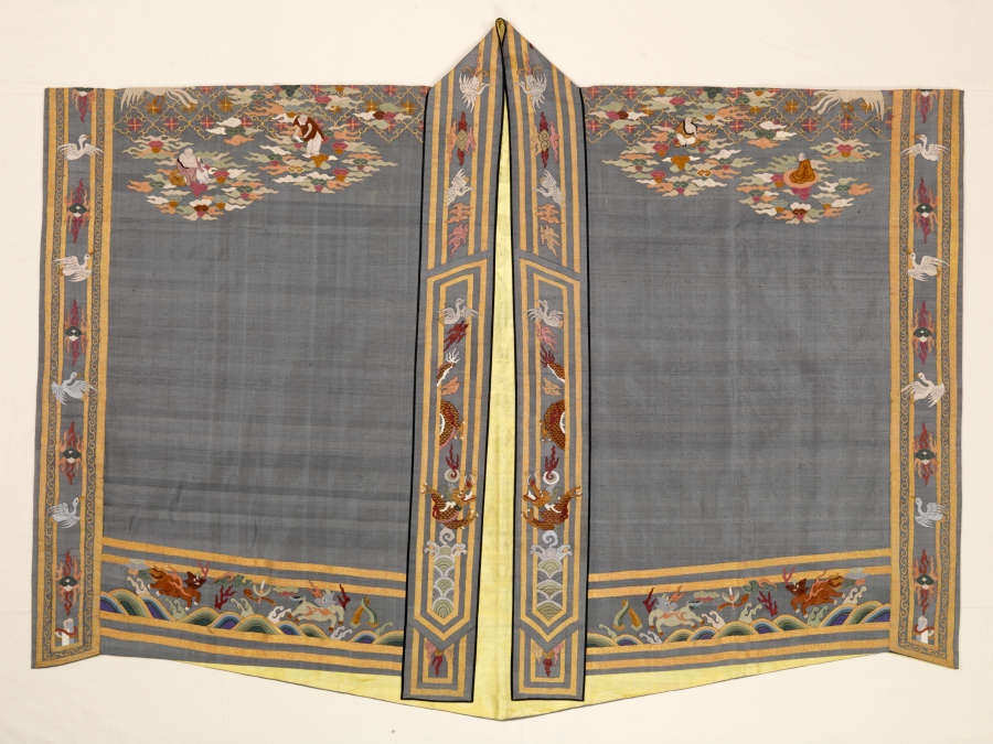 Gray-blue robe with a golden lining, laid flat. Two lapped sleeves meet at a long collar with illustrations within its borders. Each sleeve’s top-edge features illustrations continuing to the back.