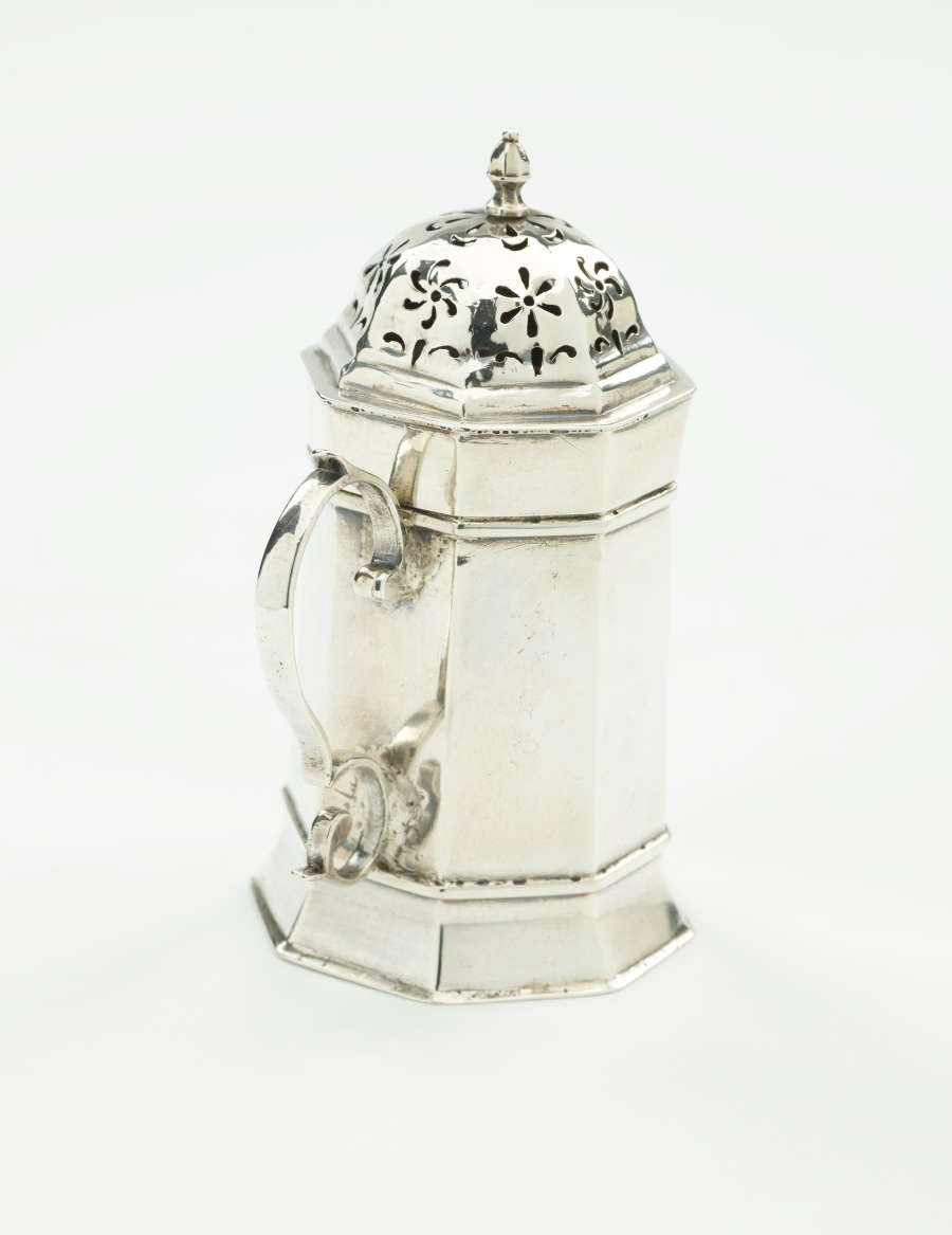  A silver vessel that has an octagonal body, handle, and lid that has floral perforations.
