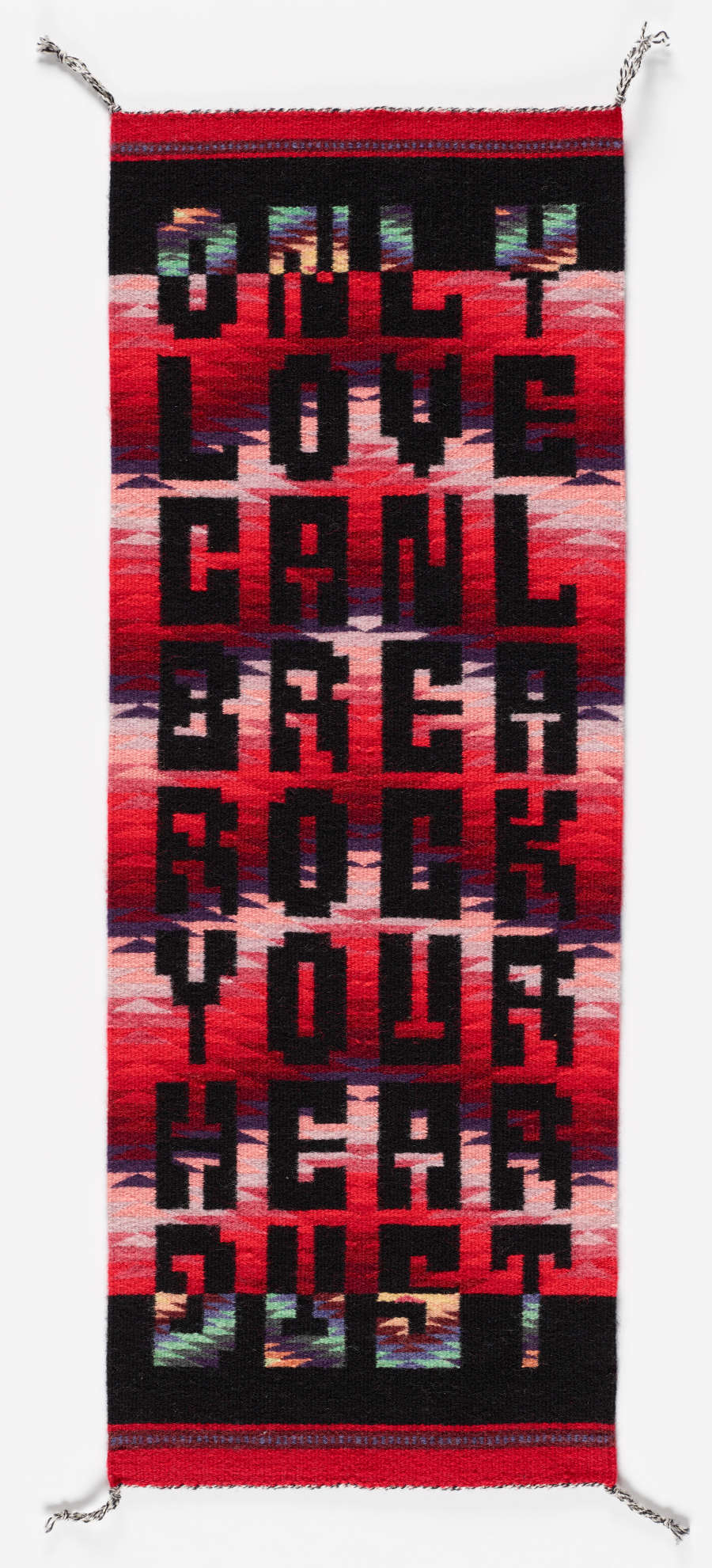 Narrow black and red woven tapestry with red and pink chevron patterning in the center and eight rows of one-worded black text which reads “only love canl brea rock your hear dust” 