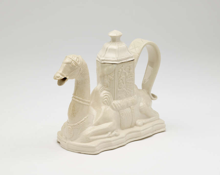 A cream colored teapot in the shape of a camel with a hexagonal lid
