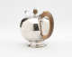 A bulbous silver teapot with a wooden finial and handle connected with decorative silver pieces. There are delicate engraved marks on the body and lid.