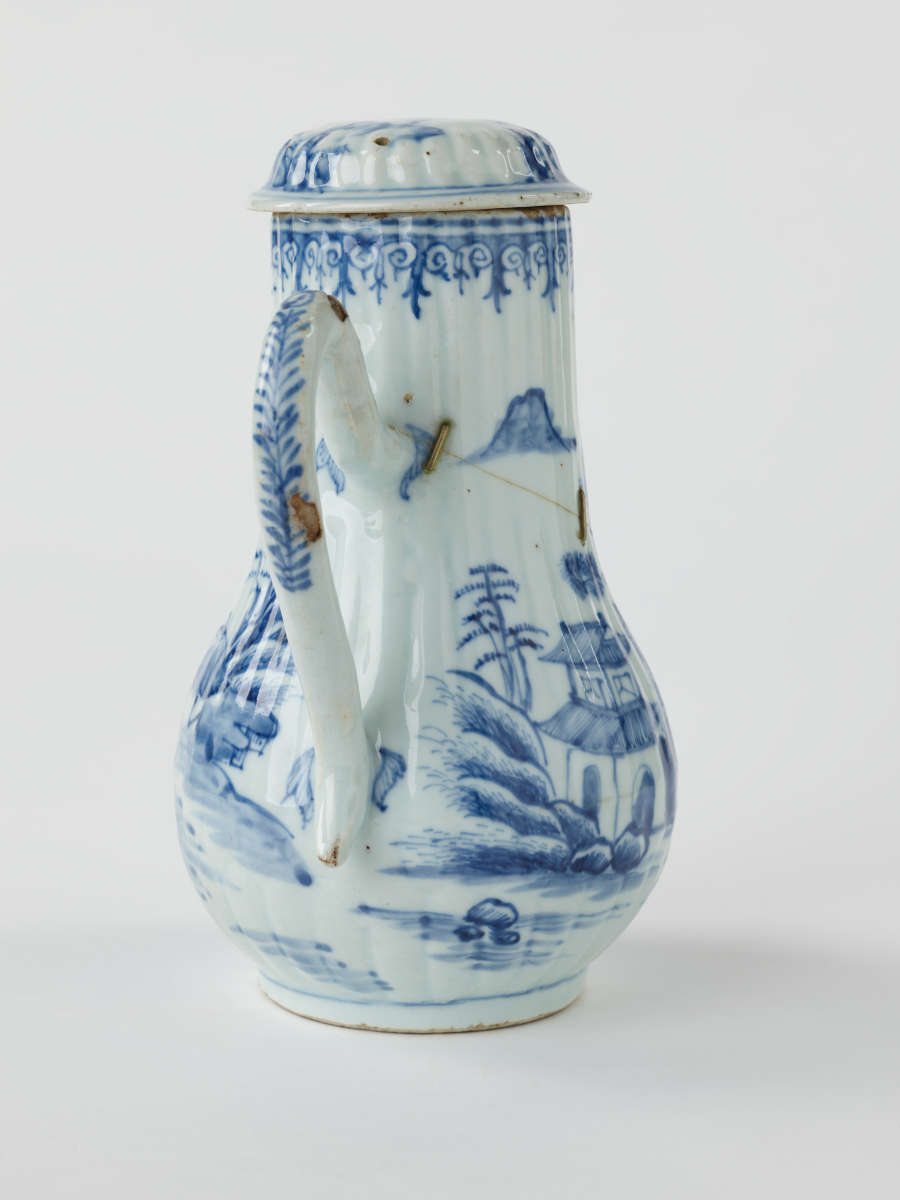 A white chocolate pot with blue decorations depicting floral and architectural elements.