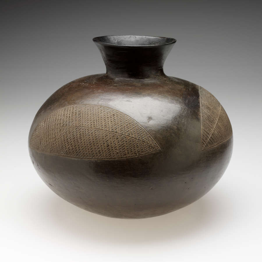 A bulbous vessel with a rounded, flared neck. Two large, abstract leaf-shaped designs are scratched into the shiny surface.
