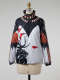 Windbreaker on a mannequin. The windbreaker features a black angular design at the top and red-orange feather and shell-motifs. The bottom is white with the silhouette of an antlered animal.