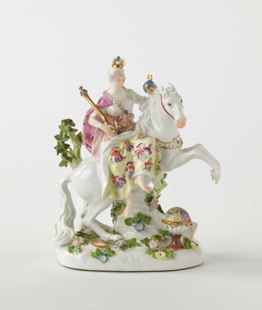 A sculptural figure on a rearing horse in historical clothing that is yellow, pink, and white with floral decorations. The figure is holding a staff and ball.