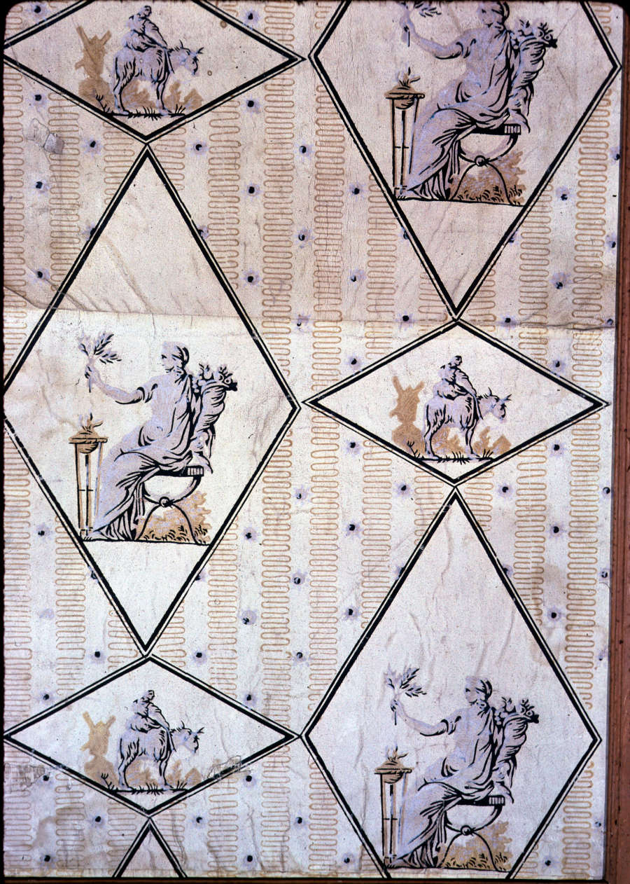 Crinkled, yellow wallpaper with repeating figures, sitting and riding a horse, enclosed in rotated diamond frames, against vertical stripes made out of yellow wavy lines and black-dotted white sections.