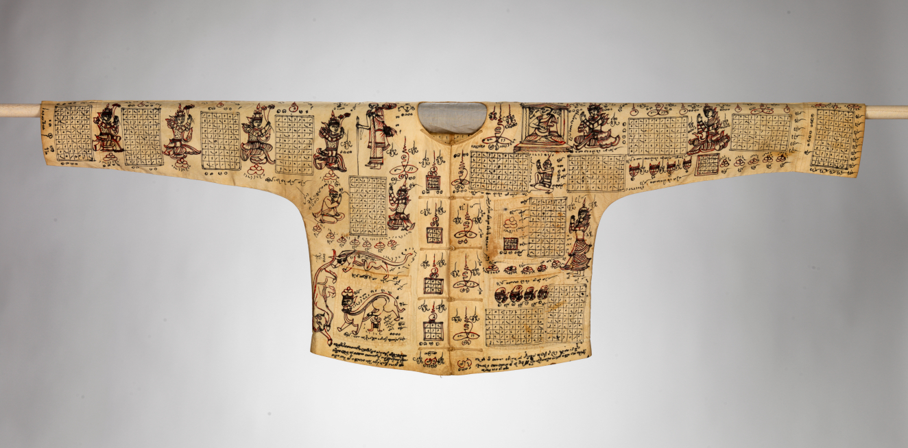 Full-view of the yellowed shirt’s front, densely populated with illustrations of mythical characters, grids and symbolic writing. It has a placket secured by ties and a round collar.