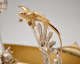 Detail of a golden bird with short beak and outstretched wings perched as if ready to fly upon  silver wheat stalks decorating an ornate scroll. 